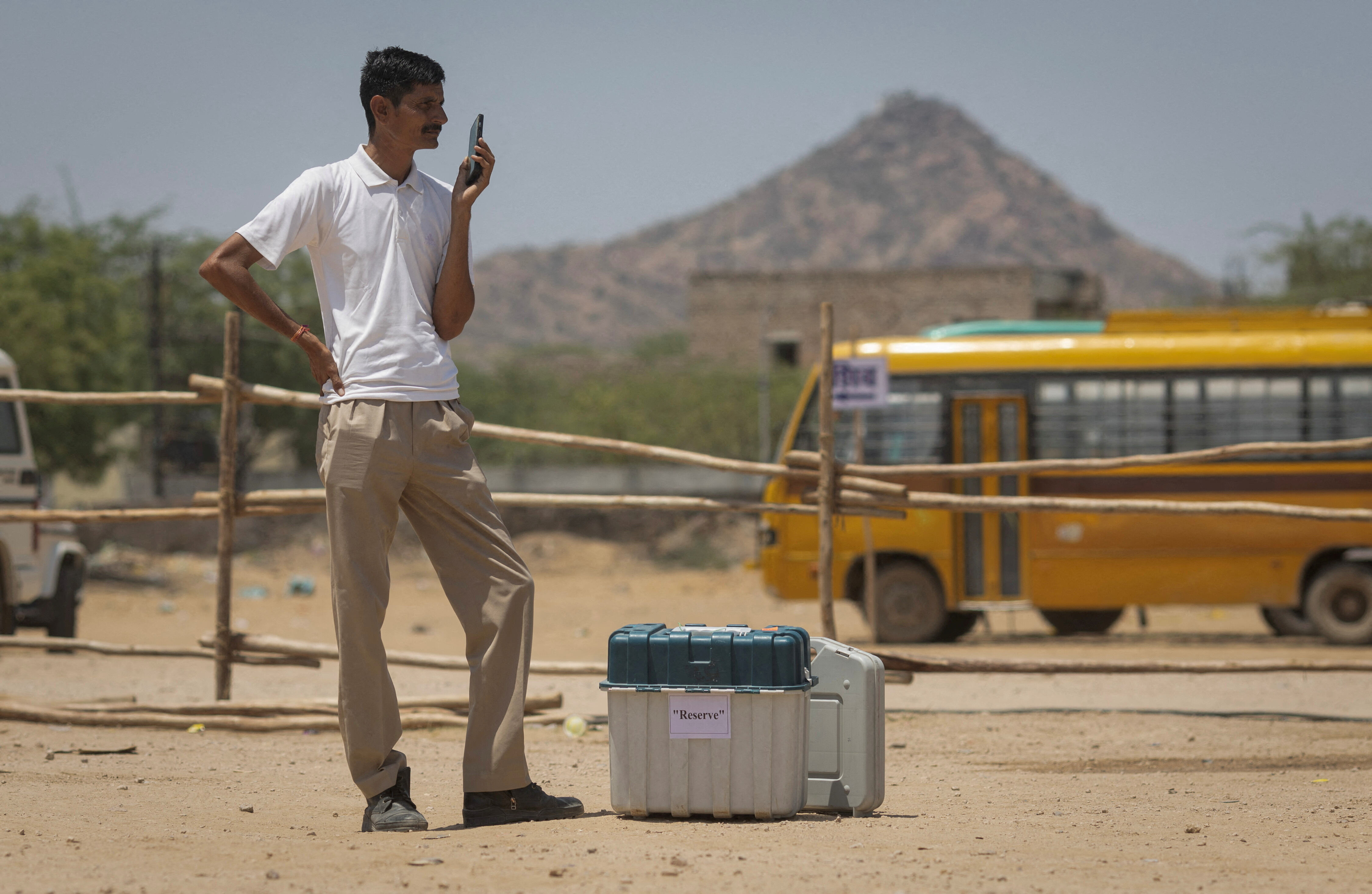 A polling officer stands next to Voter Verifiable Paper Audit Trail (VVPAT) and Electronic Voting Machines (EVM) as he wait for his colleagues at a distribution centre, ahead of the second phase of the general elections, in Barmer in the desert state of Rajasthan, India, April 25, 2024. REUTERS/Adnan Abidi